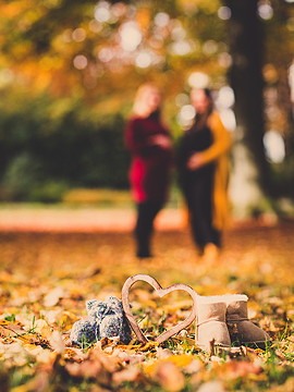 zwei schwangere Frauen im Hintergrund, vorne dran Babyschuhe mit Herz